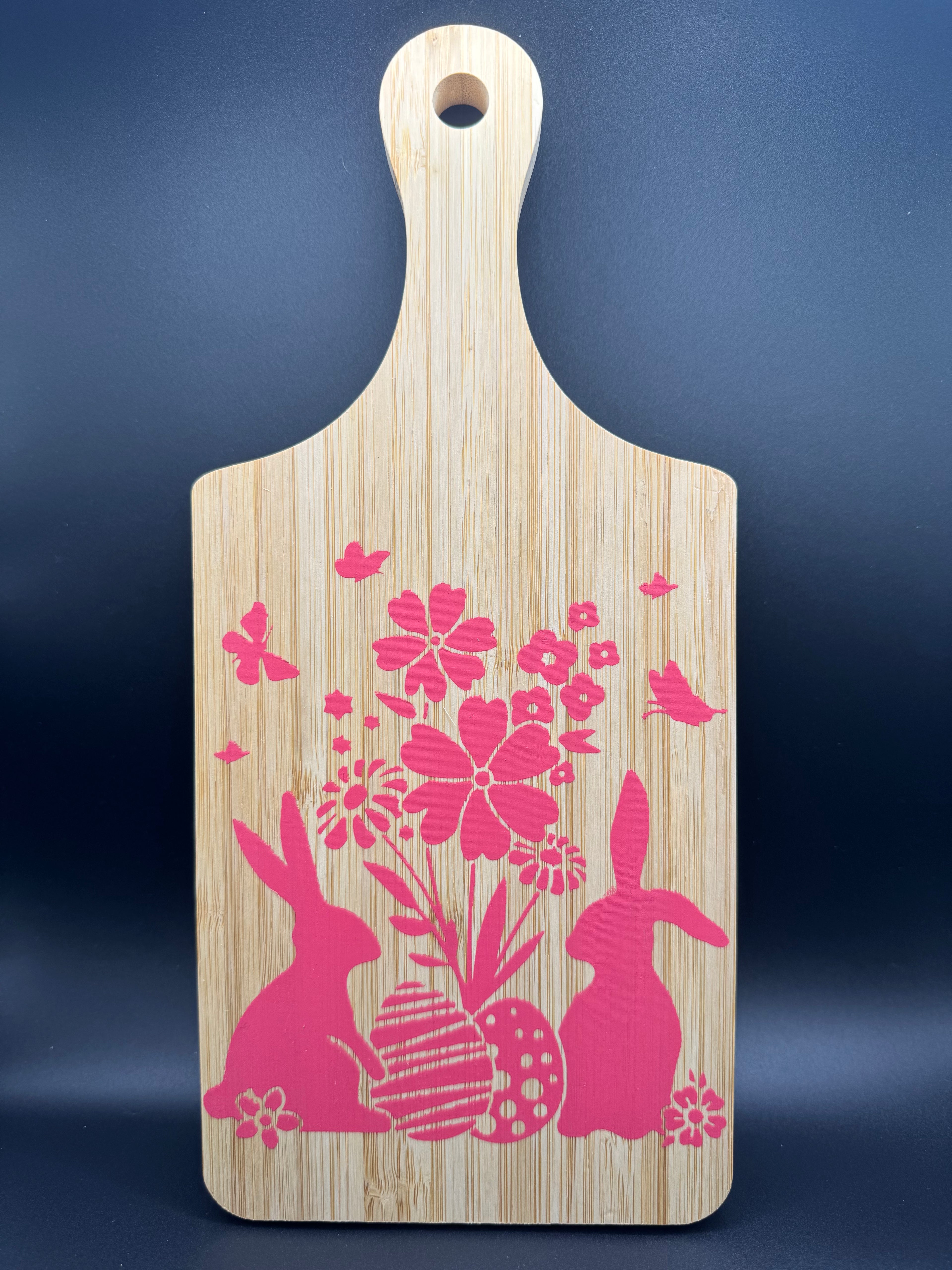 Wooden cutting board with pink floral and bunny designs on a dark blue background