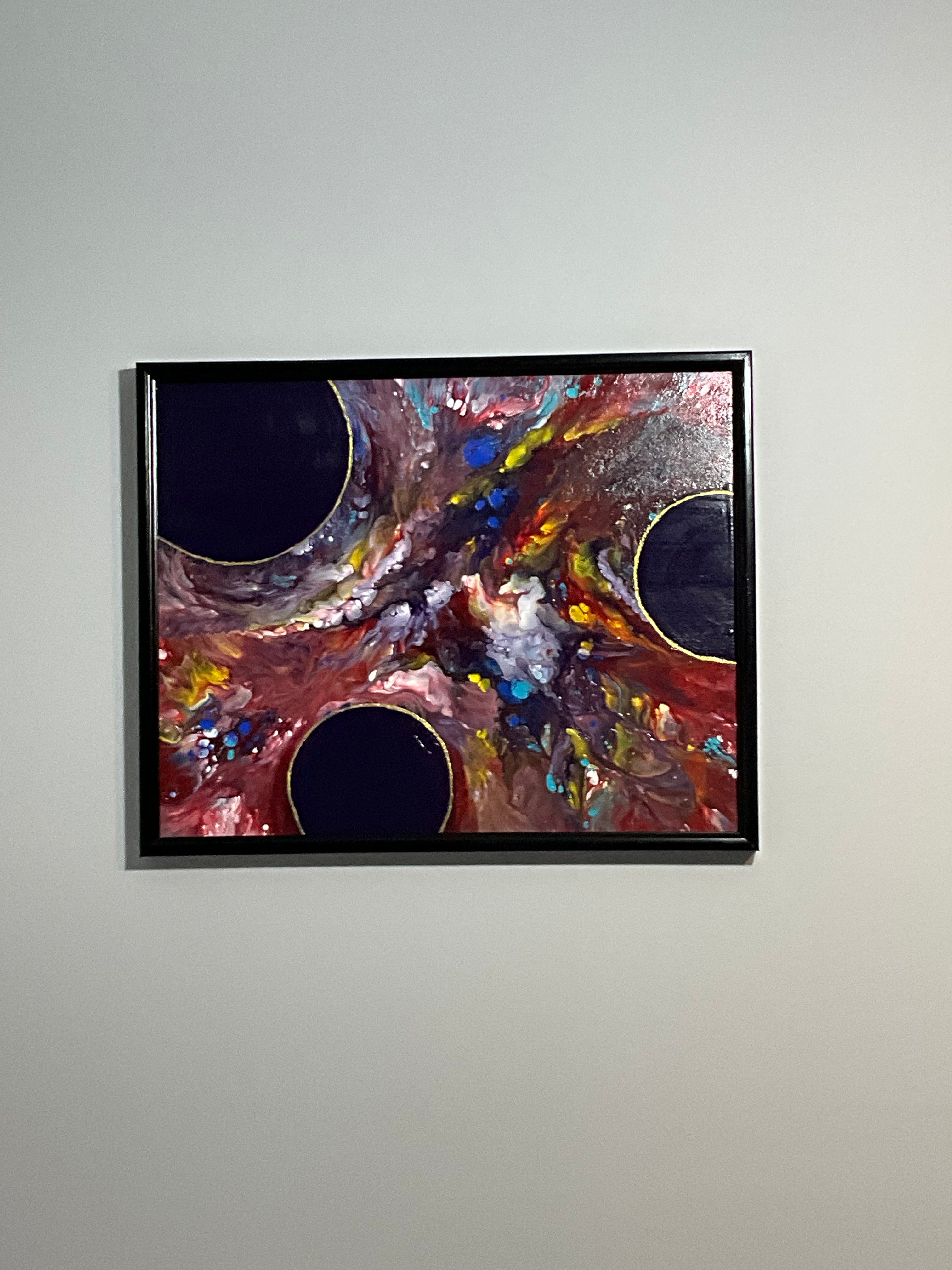 Abstract painting with colorful swirls in a black frame on a light gray wall